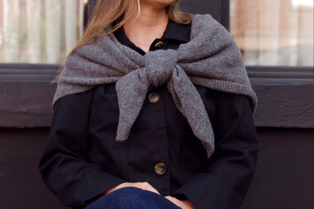 Woman wearing a gray scarf and dark coat sitting on a bench.