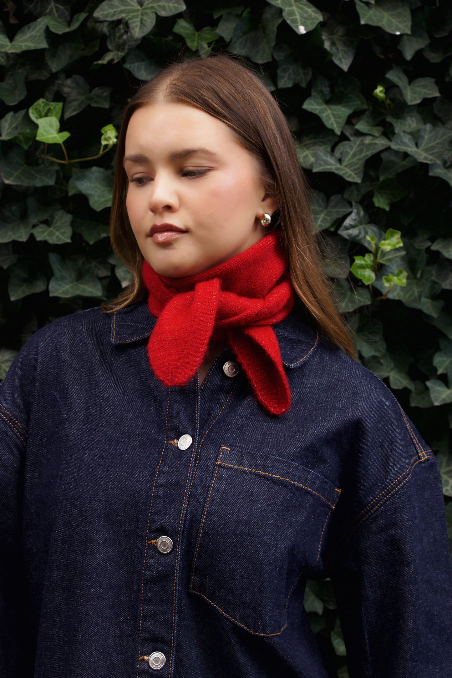 Woman wearing a red scarf and dark denim jacket against a green leafy background