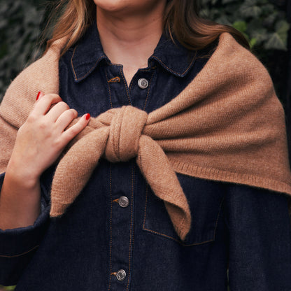 Dark denim jacket with a beige shawl scarf over her shoulders against a green leafy background in new york city.