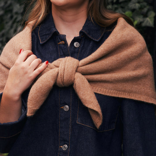 Dark denim jacket with a beige shawl scarf over her shoulders against a green leafy background in new york city.