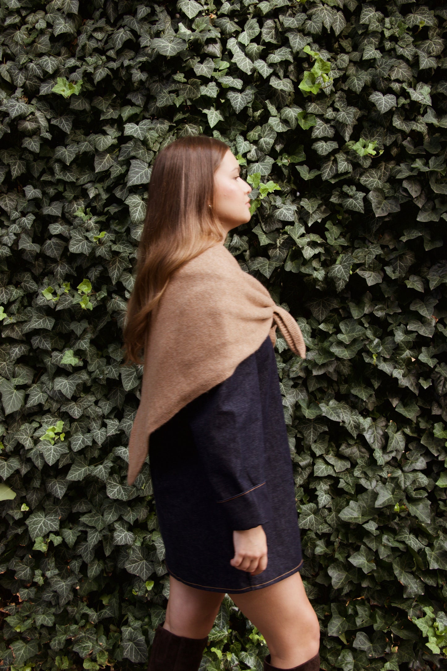 Woman wearing a beige shawl against a green leafy wall
