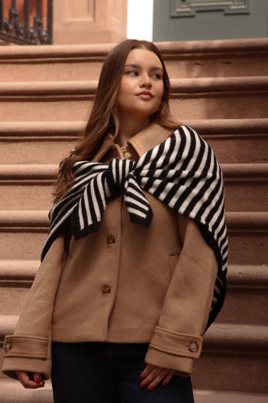Woman wearing a beige coat and black and white striped scarf on a set of brown steps.