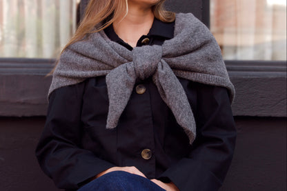 Woman wearing a gray scarf and dark coat sitting on a bench.