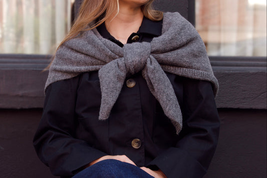Woman wearing a gray scarf and dark coat sitting on a bench.
