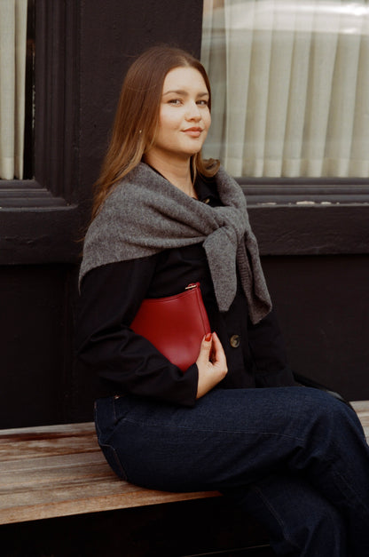 Woman sitting on a bench wearing a dark coat and gray scarf, holding a red bag.